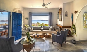 Ein Wohnzimmer mit Meerblick, einer blauen Tür und einem Deckenventilator.
