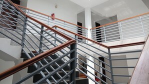 Moderni portaikko, jossa on metallikaiteet ja puiset käsijohteet, johtaa korkealle kattoon, jossa on kattovalokuvioita.