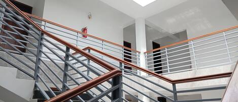 A modern staircase with metal railings and wooden handrails, leading to a high ceiling with skylights.