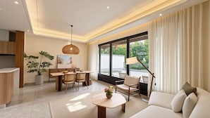 Un salon moderne comprenant un canapé, une table à manger, des chaises, un luminaire suspendu et une grande fenêtre avec des rideaux.