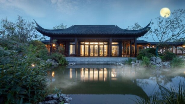 Un bâtiment traditionnel chinois, avec un bassin devant, entouré de verdure.