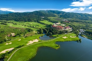 A golf course with a large building surrounded by water and hills.