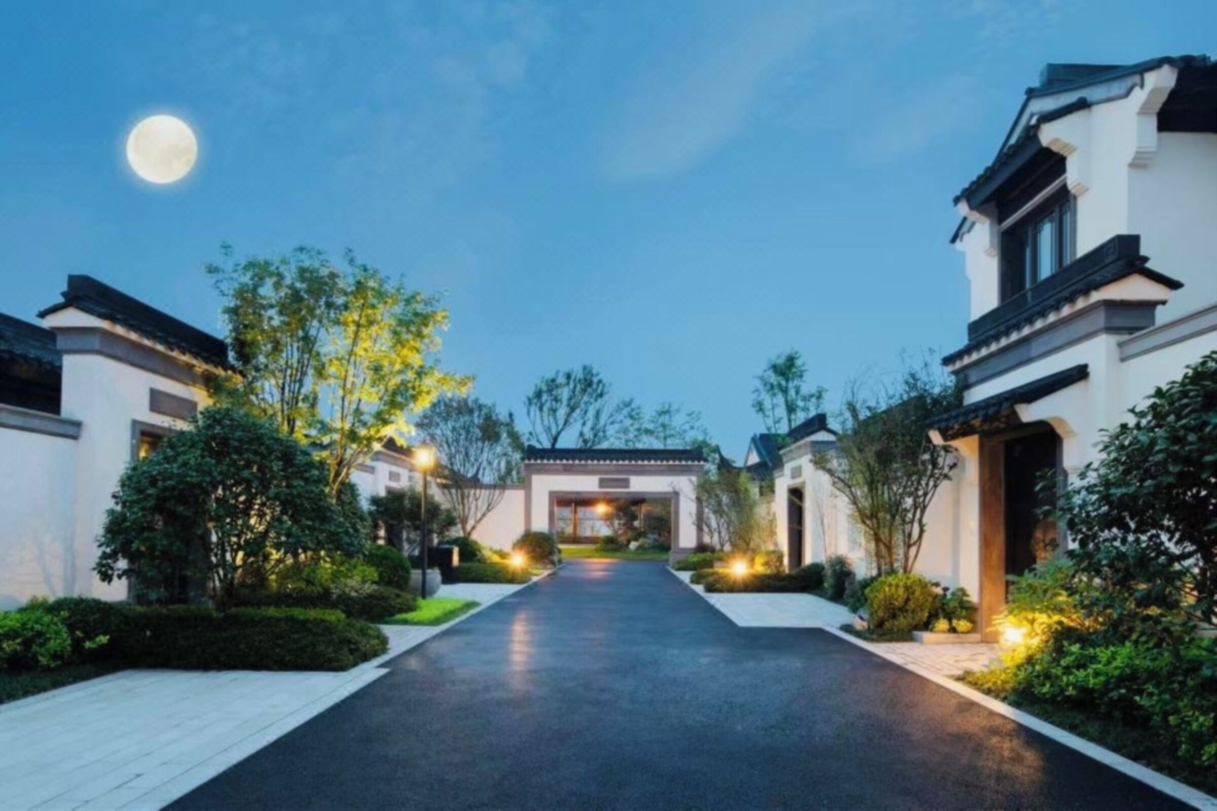 A pathway leading to a building with a traditional architectural style, surrounded by greenery and illuminated by street lamps.
