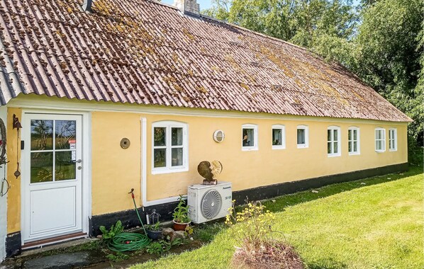 Une maison jaune avec un toit en tuiles, une porte blanche et un jardin avec de la pelouse et des plantes.