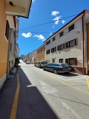 Eine enge Straße mit parkenden Autos, Häusern an beiden Seiten und blauem Himmel.