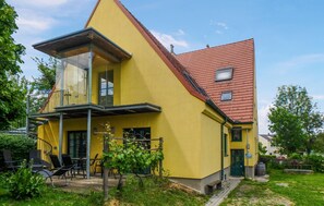 Ein gelbes, zweistöckiges Haus mit rotem Dach, einem Balkon und einem kleinen Garten mit Sitzgelegenheiten.