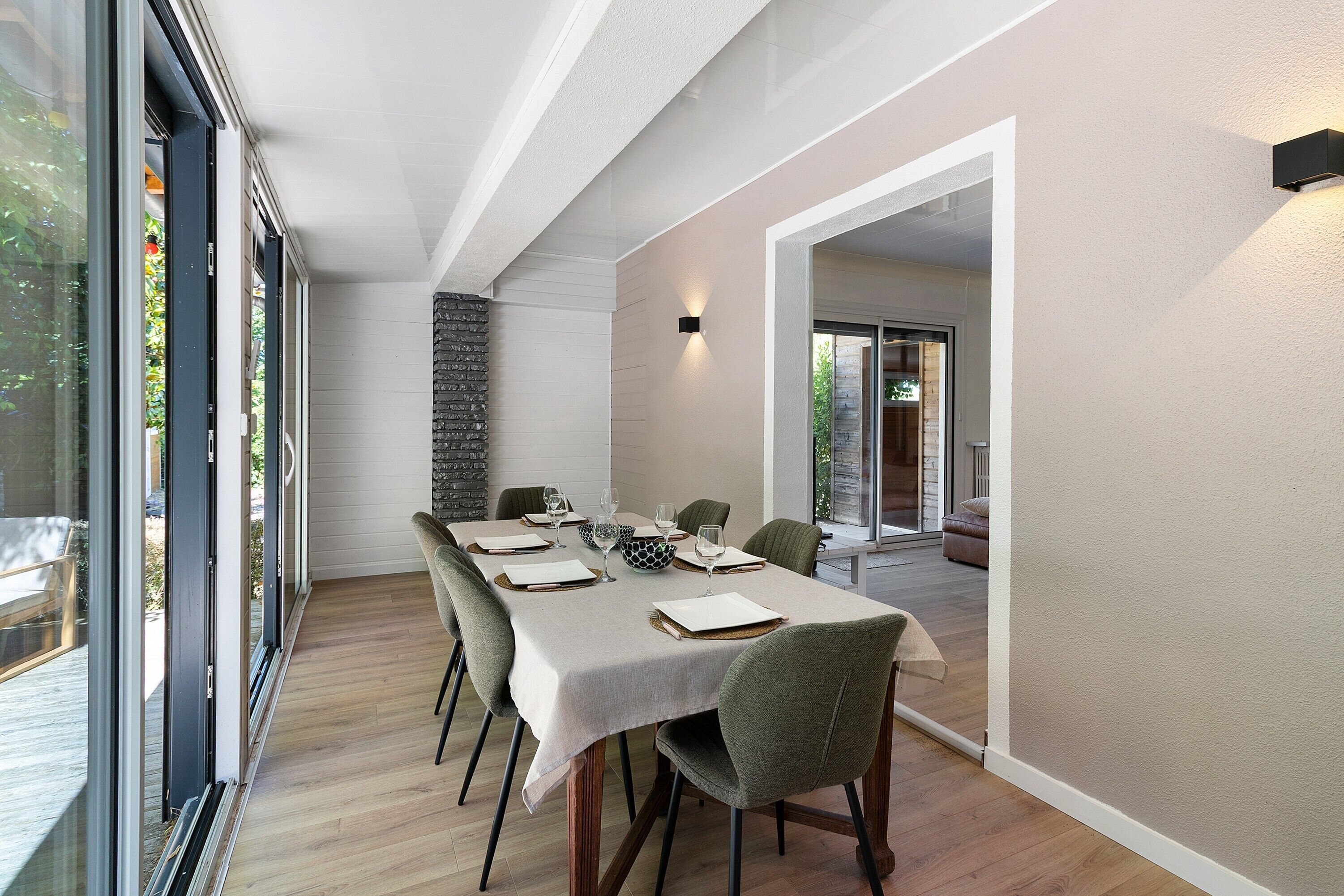 A dining area with a table set for six, a stone accent wall, and a view through glass doors.