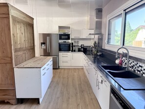 A modern kitchen with white cabinetry, stainless steel appliances, a wooden countertop, and a large window.