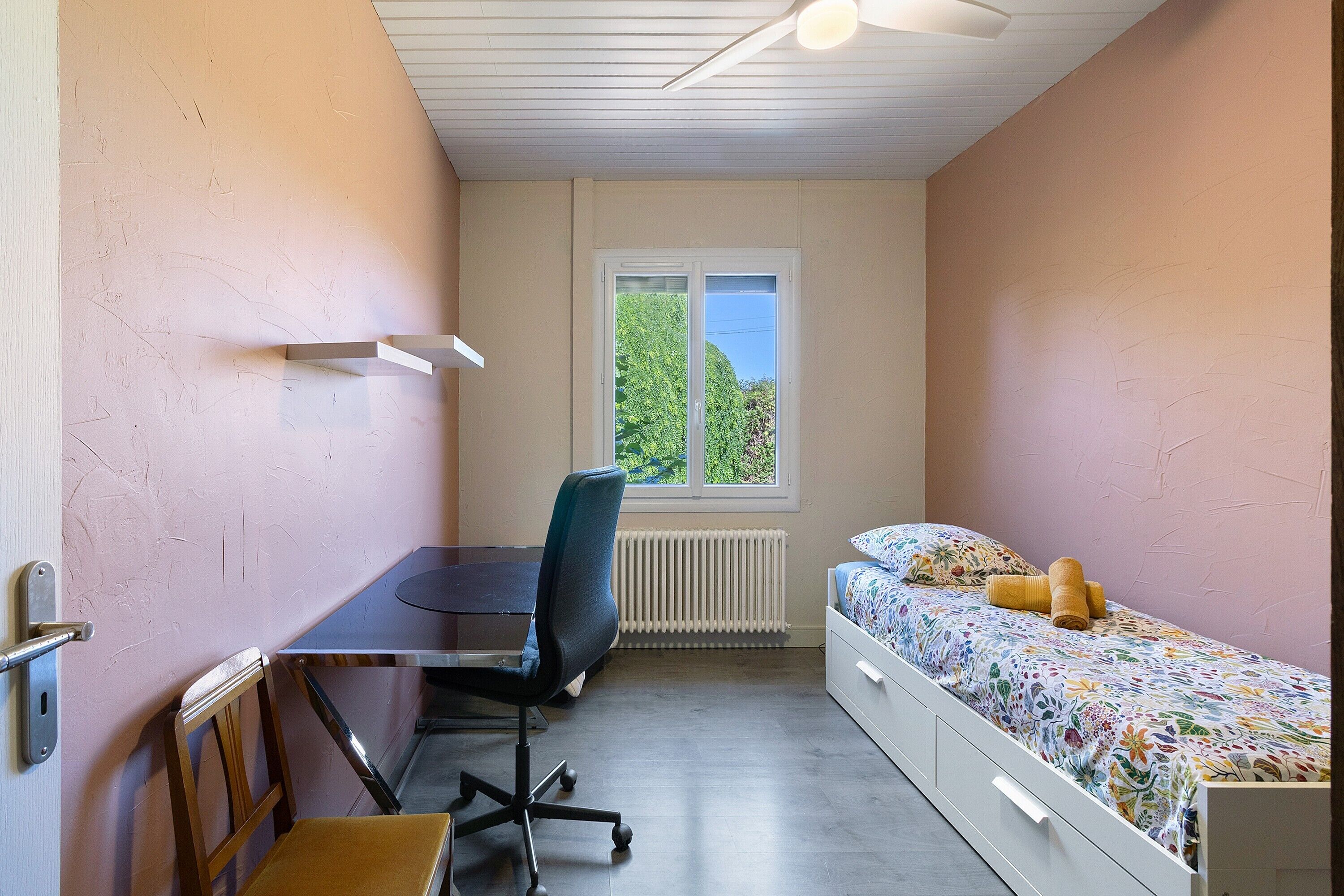 A room with a desk, chair, bed, and a window with a view.