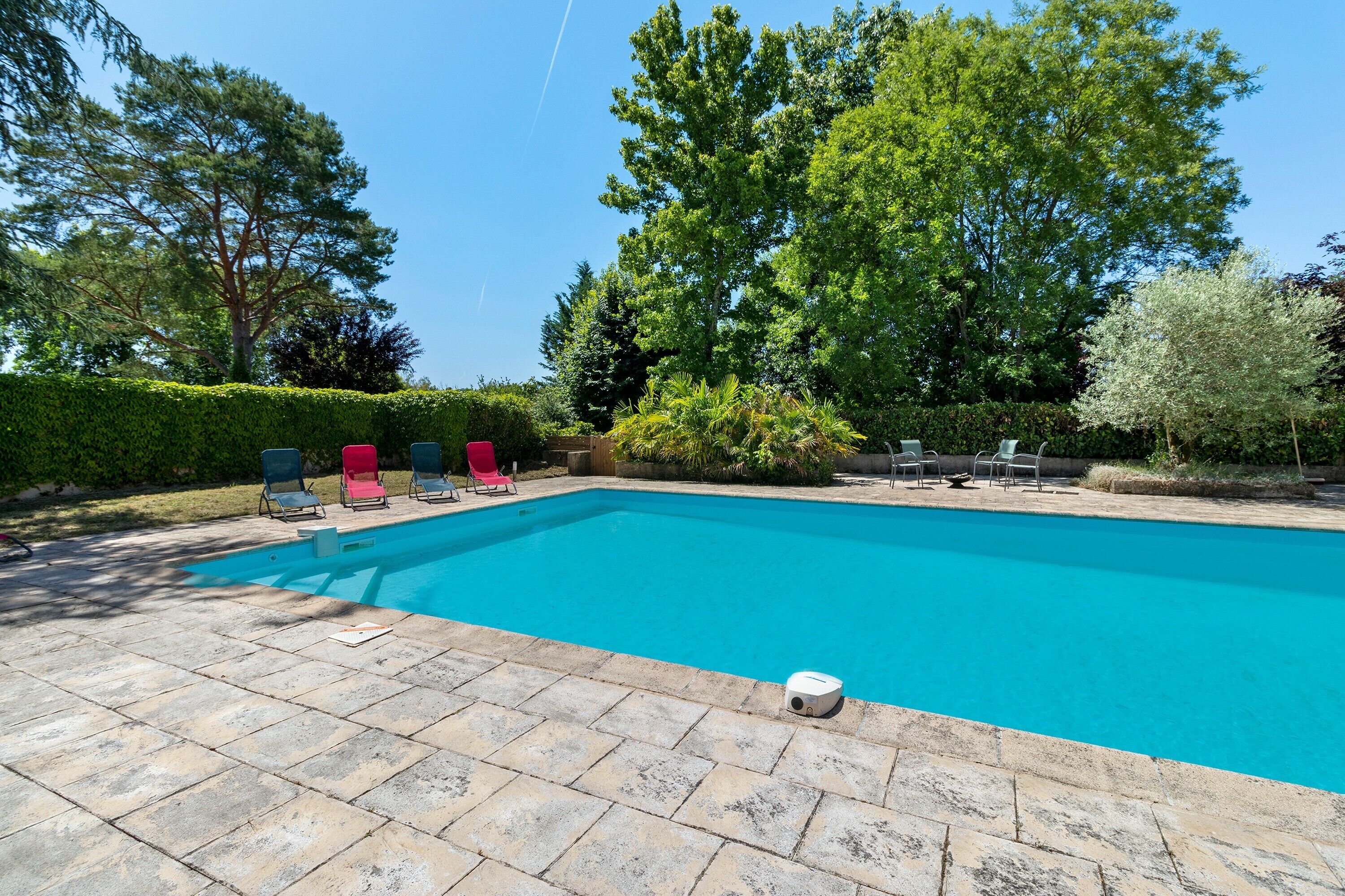 Une piscine dotée d’une terrasse carrelée, entourée de verdure et d’arbres.