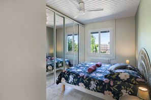 A bedroom with a bed, a mirror, a window, and a ceiling fan.