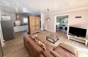 A modern living room with a sofa, coffee table, TV, and kitchen area with cabinets and appliances.