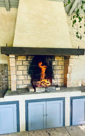 Une cheminĂ©e en briques avec un feu qui crĂ©pite Ă lâintĂ©rieur, une Ă©tagĂšre en mĂ©tal au-dessus et un rebord en bĂ©ton en dessous.