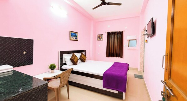 A pink-themed hotel room with a bed, desk, chair, ceiling fan, and a TV. - Hotel Jagannath Inn Puri (Puri)