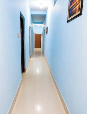 A long, narrow hallway with light blue walls and a tiled floor, leading to a wooden door at the end. - Hotel Jagannath Inn Puri (Puri)