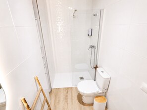 A modern bathroom with a glass-enclosed shower, a toilet, and a wooden floor. - CREA Conil Apartments IV (Conil de la Frontera)