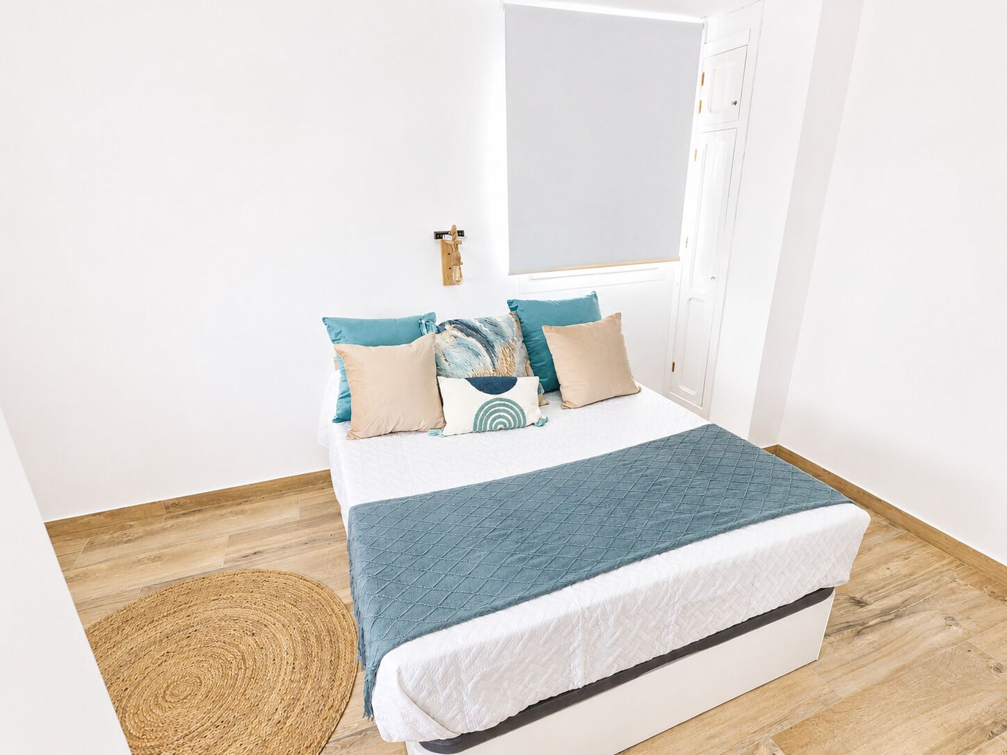 A bed with a quilted blue blanket, a woven rug, and a wooden floor.