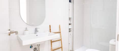 A modern bathroom with a white sink, mirror, toilet, and shower.