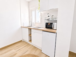 Eine kompakte Küche mit weißen Schränken, einer Holz Arbeitsplatte, einer eingebauten Mikrowelle und einem Spülbecken.