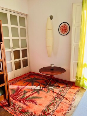A room with a round table, a surfboard decoration, a patterned rug, and a door with frosted glass panels.