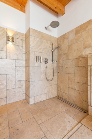 Un espace douche avec des carreaux de pierre, une douchette à main, un robinet mural et une pomme de douche fixée au plafond.