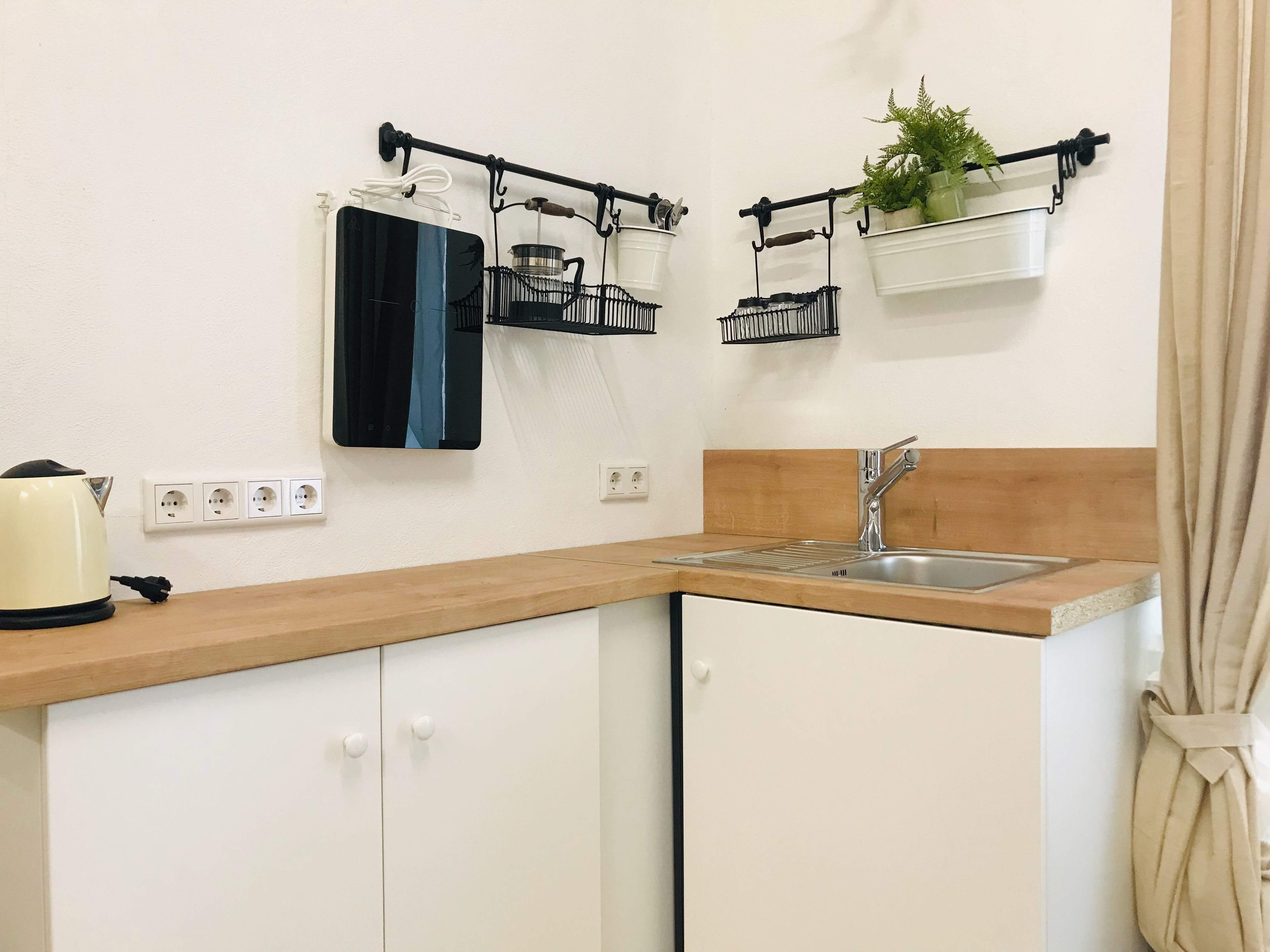 Cocina con armarios blancos, encimera de madera, un lavabo y dos cestas colgantes negras con plantas.