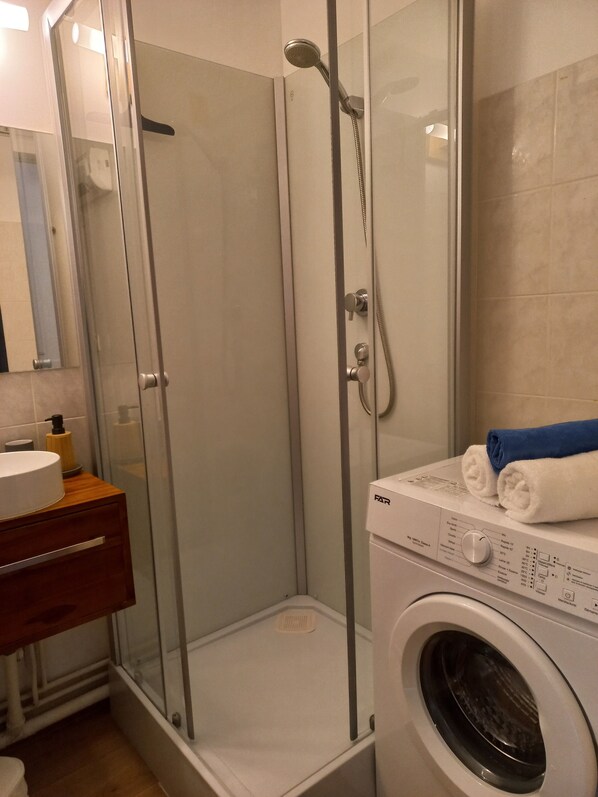 A bathroom with a glass-enclosed shower, a washing machine, and a wooden vanity.