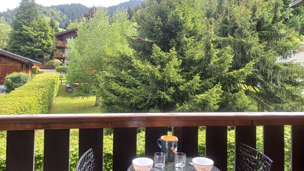 Un balcone con un tavolo apparecchiato per due, con vista su una zona boschiva e una montagna sullo sfondo.