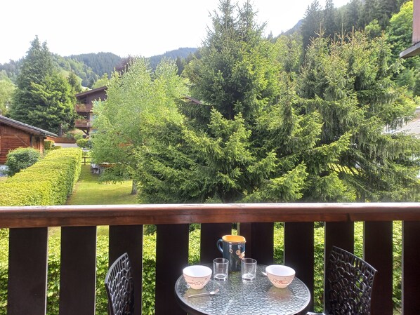 A balcony with a table set for two, overlooking a forested area with a mountain in the background.