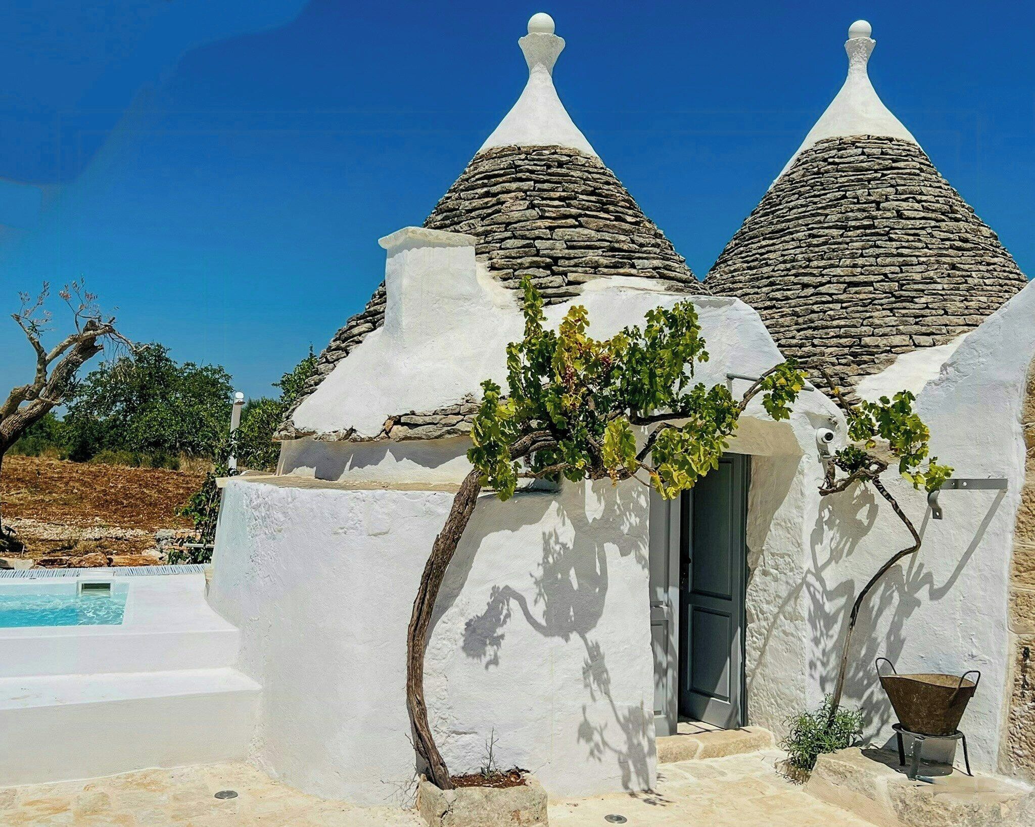 A white building with two conical roofs, a door, and a small outdoor area with a pool.