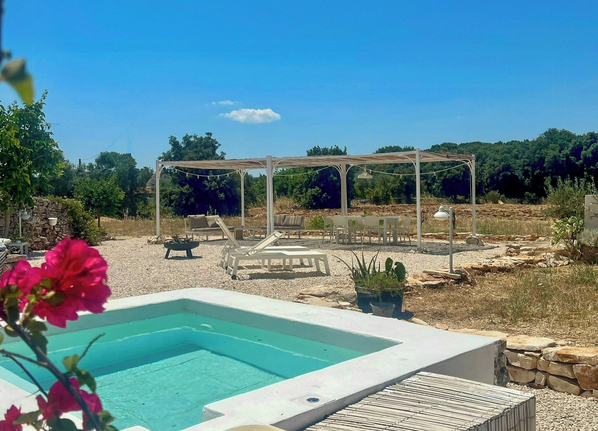 Una piscina con un pérgola, sillones de descanso y un muro de piedra.