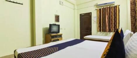 Una habitación de hotel con una cama, televisor, ventilador de techo y ventana con cortinas.