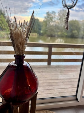 A red glass vase with dried grass on a wooden deck overlooking a body of water. - Les Rives du Bel Air (Passais-Villages)