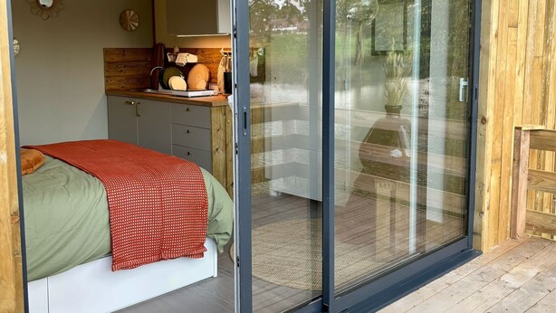 Un dormitorio con cama, cabecera de madera, puerta corredera de vidrio y vistas al exterior.