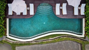 Ein Schwimmbecken mit Liegestühlen und Sonnenschirmen, umgeben von viel Grün.