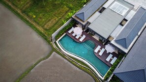 Eine Vogelperspektive zeigt ein Wohnhaus mit Schwimmbad, Liegestühlen und einer überdachten Terrasse.