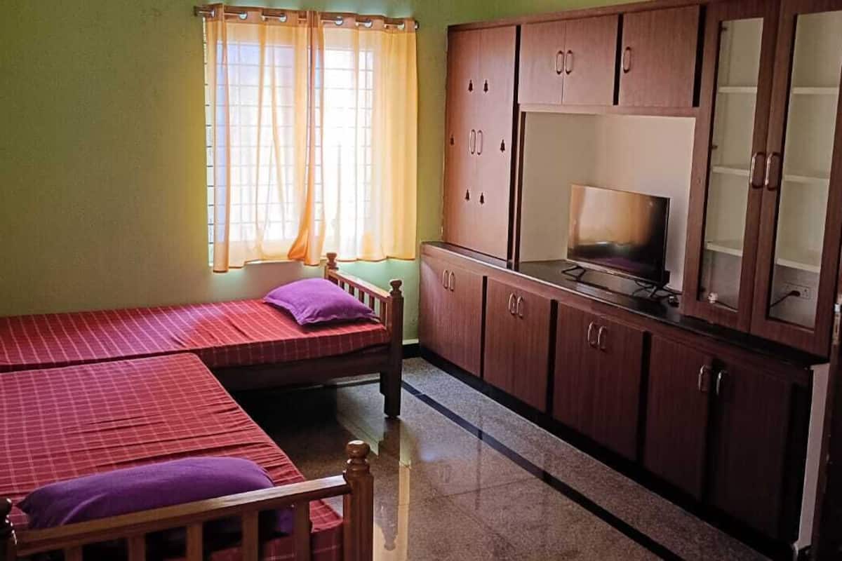 A room with two beds, a TV, wooden cabinets, and a window with curtains.
