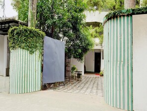 A gated courtyard with a checkered pathway, a metal gate, and a tree. - Super Deluxe Room Heaven Gardens (Kanayannur)
