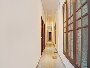 A corridor with wooden doors and windows, a tiled floor, and a ceiling with recessed lighting. - Super Deluxe Room Heaven Gardens (Kanayannur)