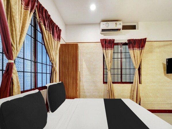 A hotel room with a bed, two chairs, a window with curtains, an air conditioning unit, and a television. - Super Deluxe Room Heaven Gardens (Kanayannur)