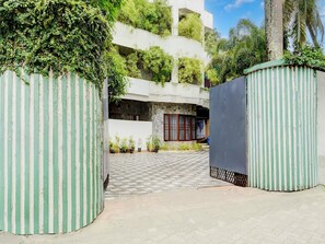 A gated entrance with a checkered pavement leading to a building with a stone facade and a window with a red frame. - Super Deluxe Room Heaven Gardens (Kanayannur)