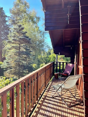 Eine Holzterrasse mit Geländer, zwei Liegestühle und Blick auf Bäume.