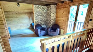 A wooden cabin interior with a staircase, two leather armchairs, a stone wall, and a wooden floor. - Chalet Cosy et Nature avec Grand Jardin & Vue Montagne | Ideal for Family and Friends (Le Ménil)