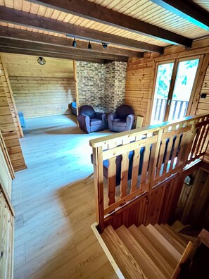 Ein Holzblockhaus mit Treppe, zwei Ledersesseln, einer Steinwand und Holzboden.