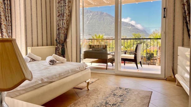 Ein Schlafzimmer mit Bett, Nachttisch, Lampe, Fenster mit Vorhängen und einem Balkon mit Stuhl und Tisch.