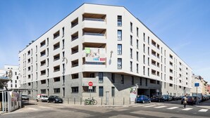 En flervåningsbyggnad med balkonger, ett övergångsställe och parkerade bilar.