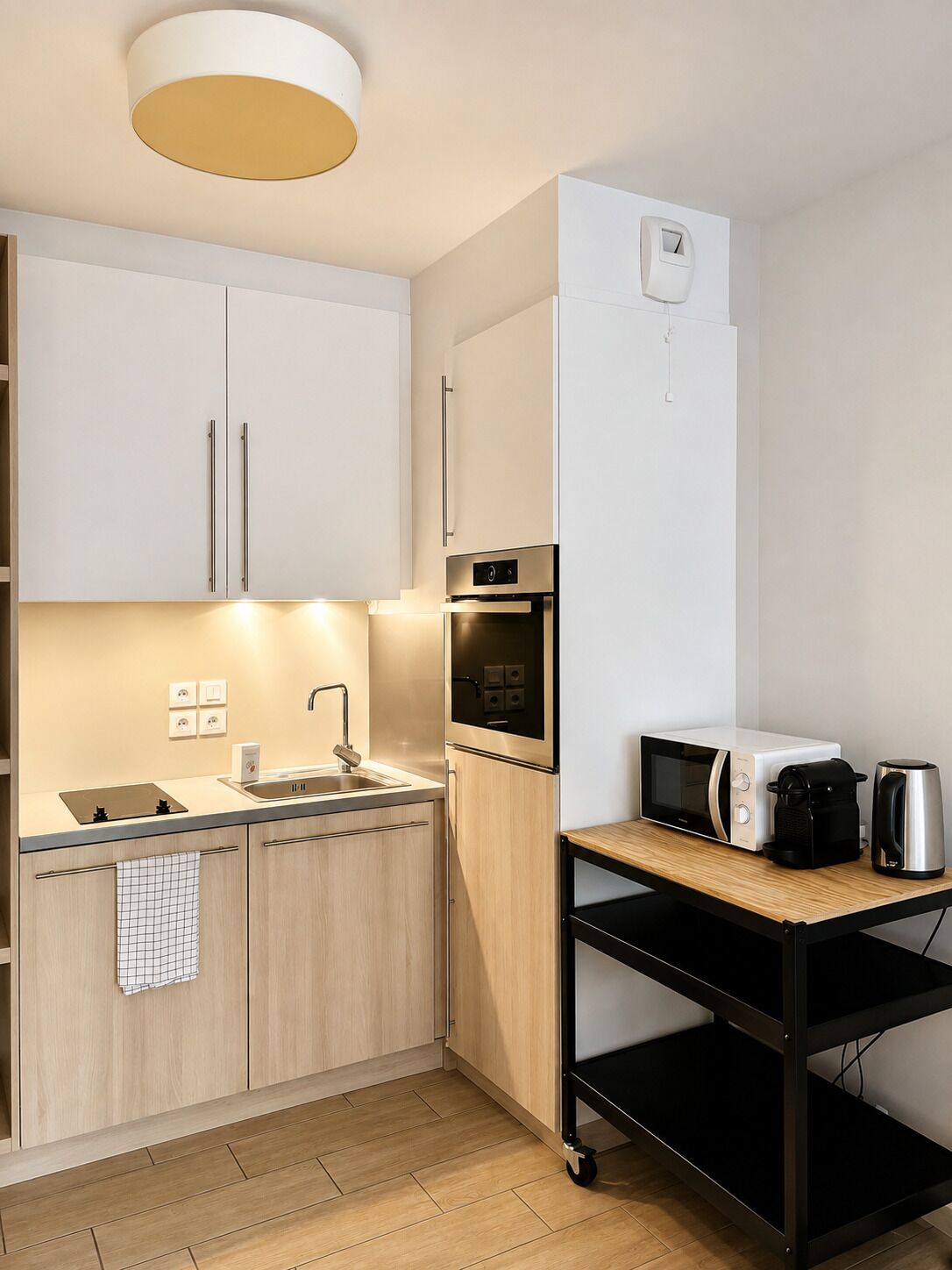 A compact kitchen with a sink, stove, microwave, and a small table with a kettle and coffee maker.