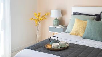 A neatly made bed with pillows, a bedside table with a lamp, and a tray with a croissant, tea cups, and a teapot.