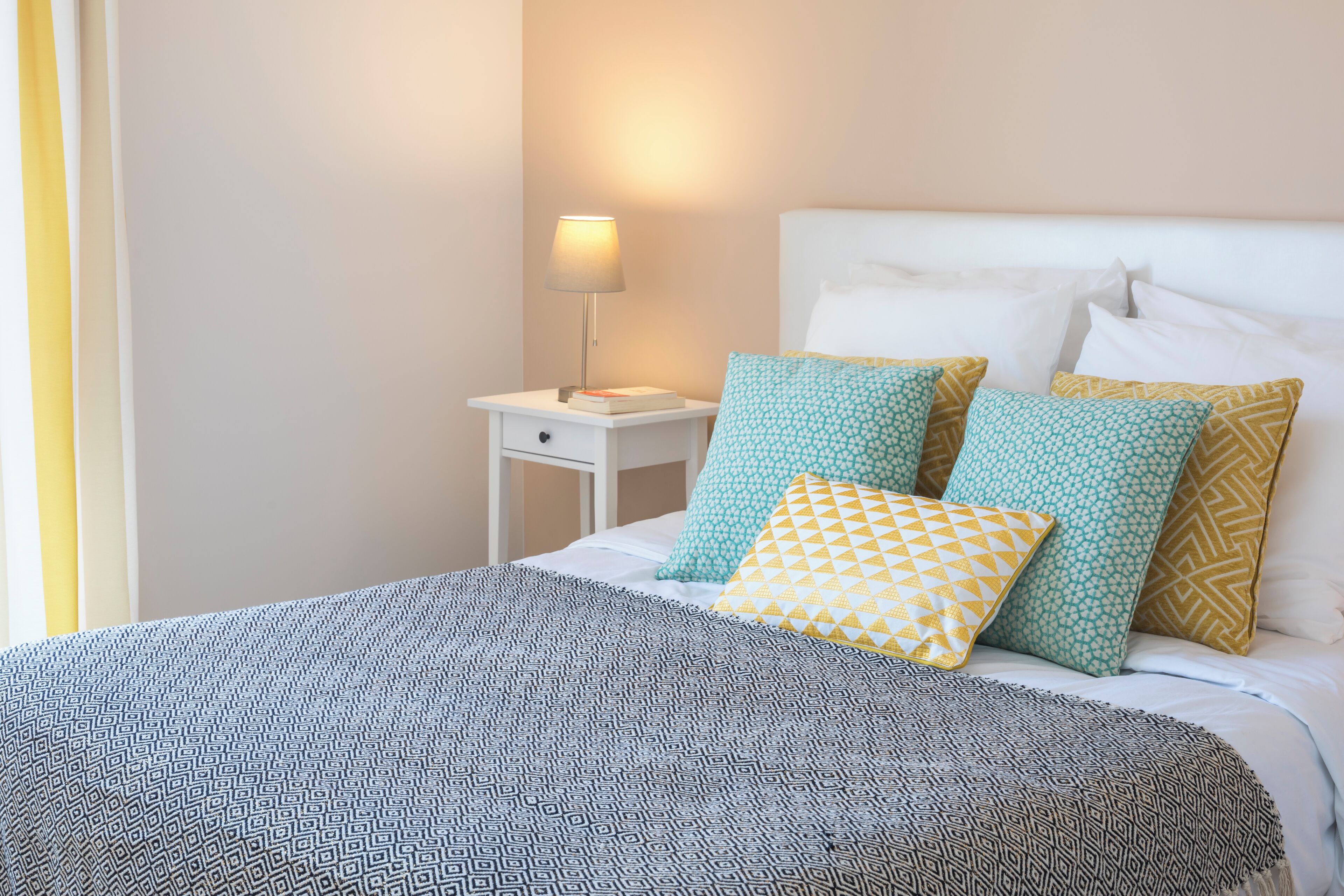 A neatly made bed with patterned bedding, a bedside lamp, and a nightstand with a book.