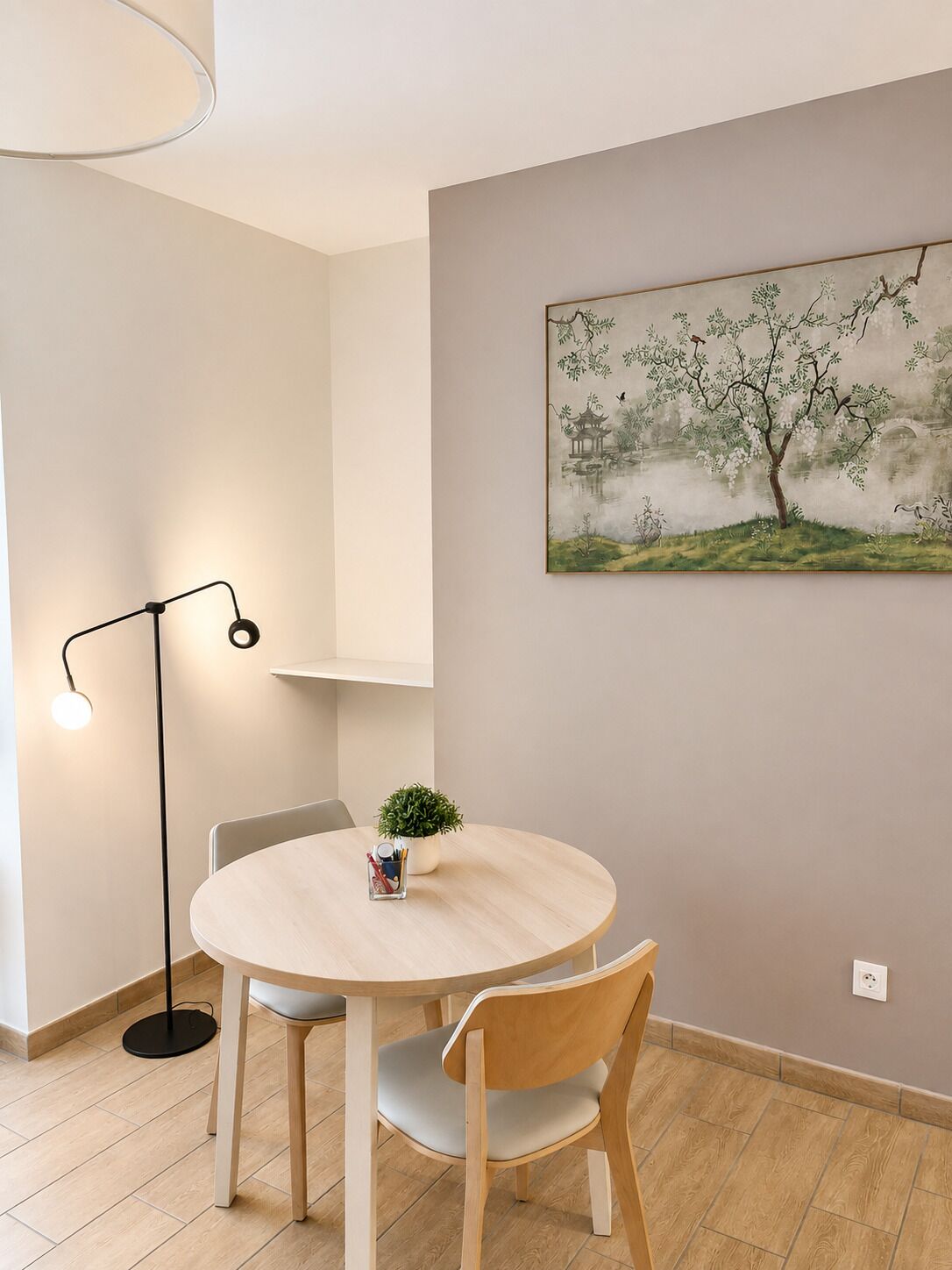 Una habitación moderna con una mesa redonda, dos sillas, una lámpara de pie y un cuadro de un árbol en la pared.